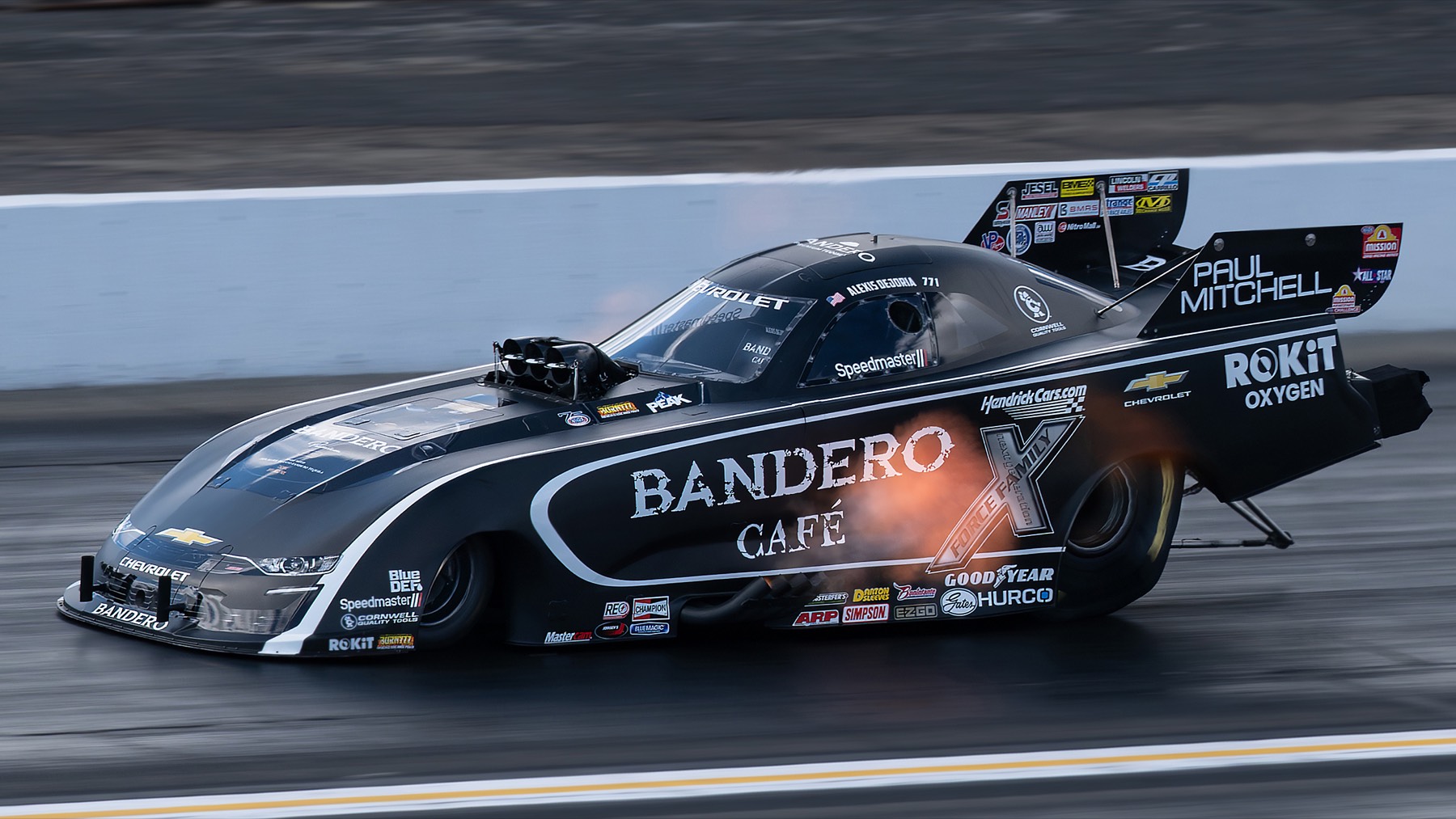 A black funny car at speed with faint flames visible at the header pipes.