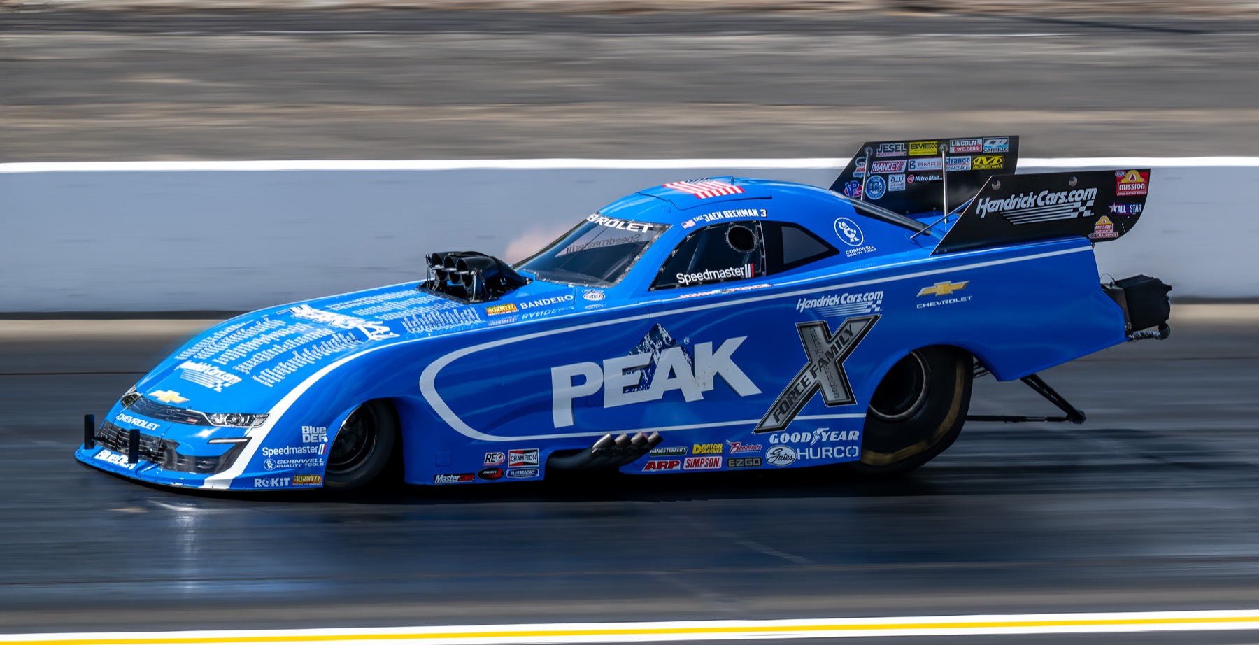 A blue funny car at speed, body down, framed against the track wall.