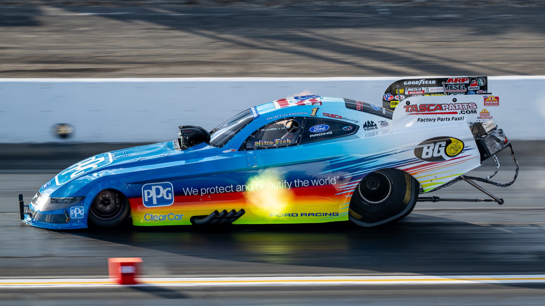 A rainbow-liveried funny car at speed in low golden-hour light.