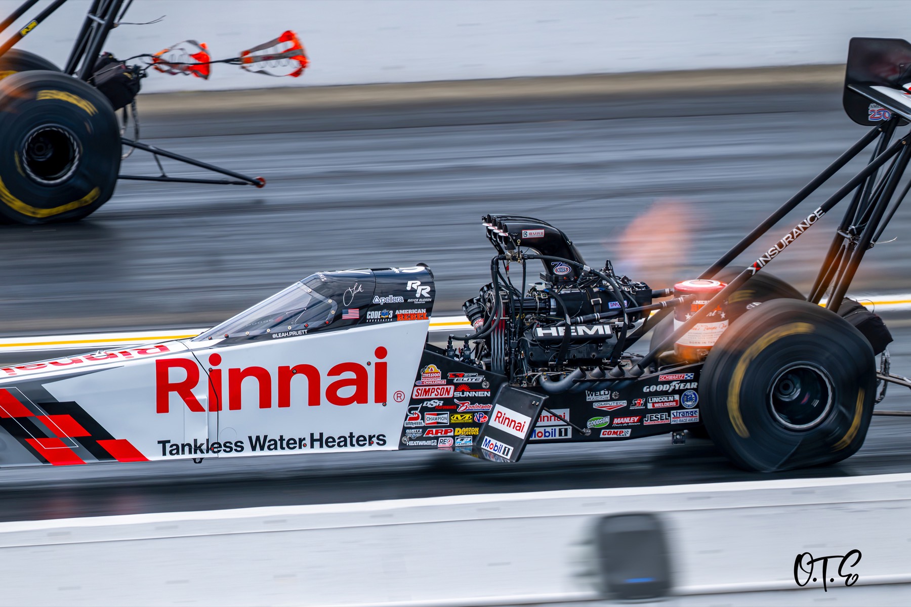A top fuel dragster under power while parachutes blossom in the far lane.