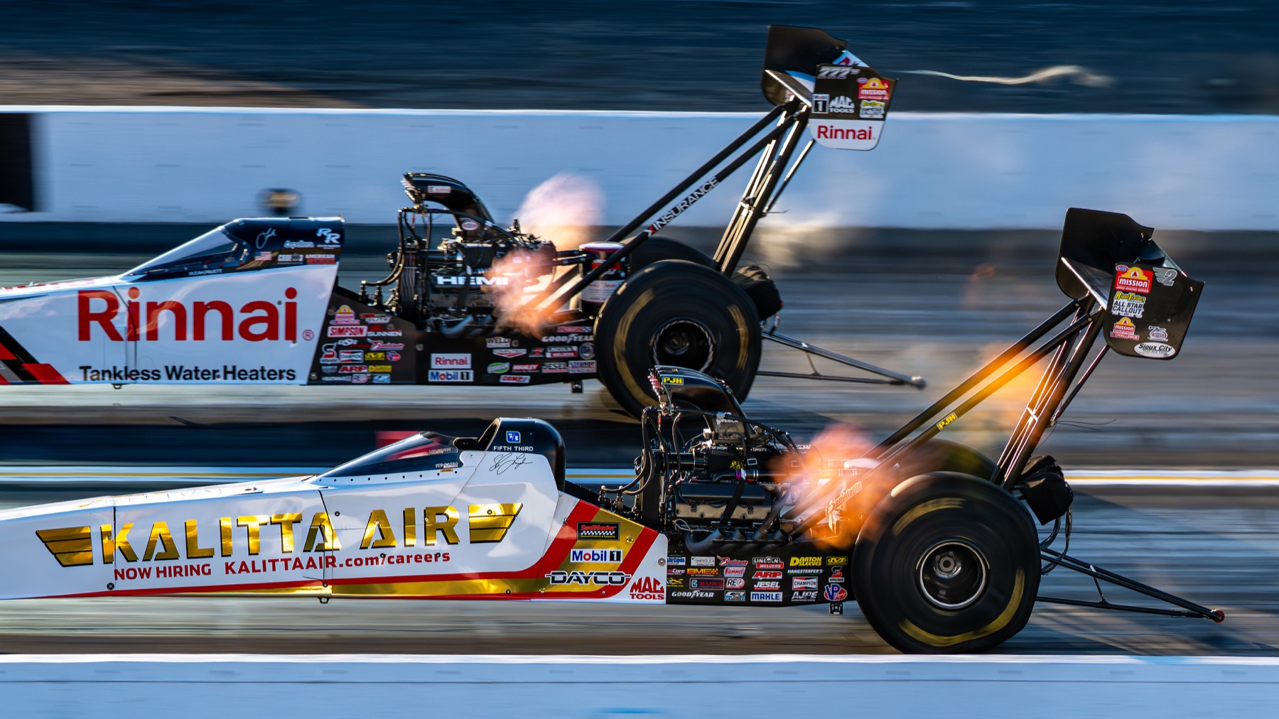 Two top fuel dragsters side by side, both engines throwing header flames.