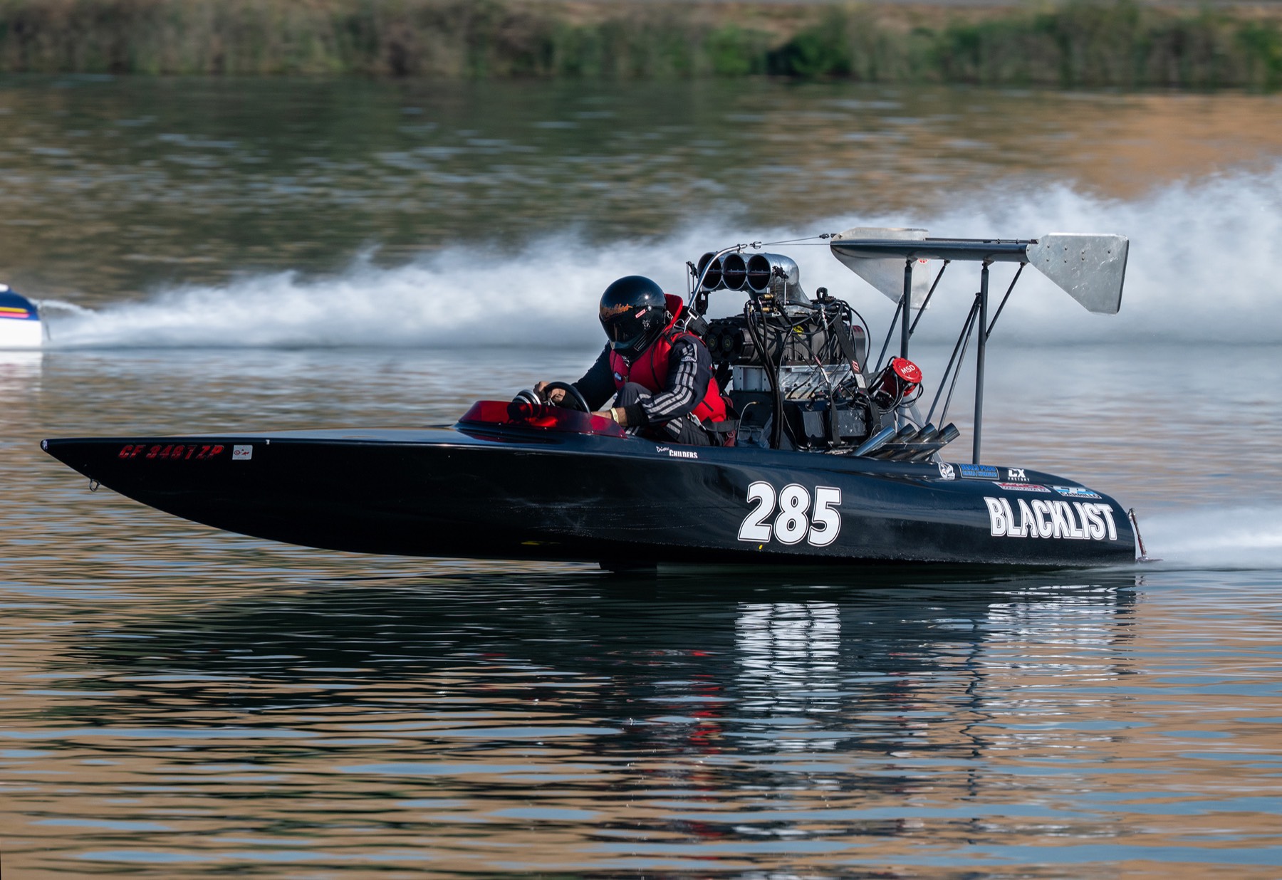 A black drag boat with a blown engine at speed, spray trailing behind.